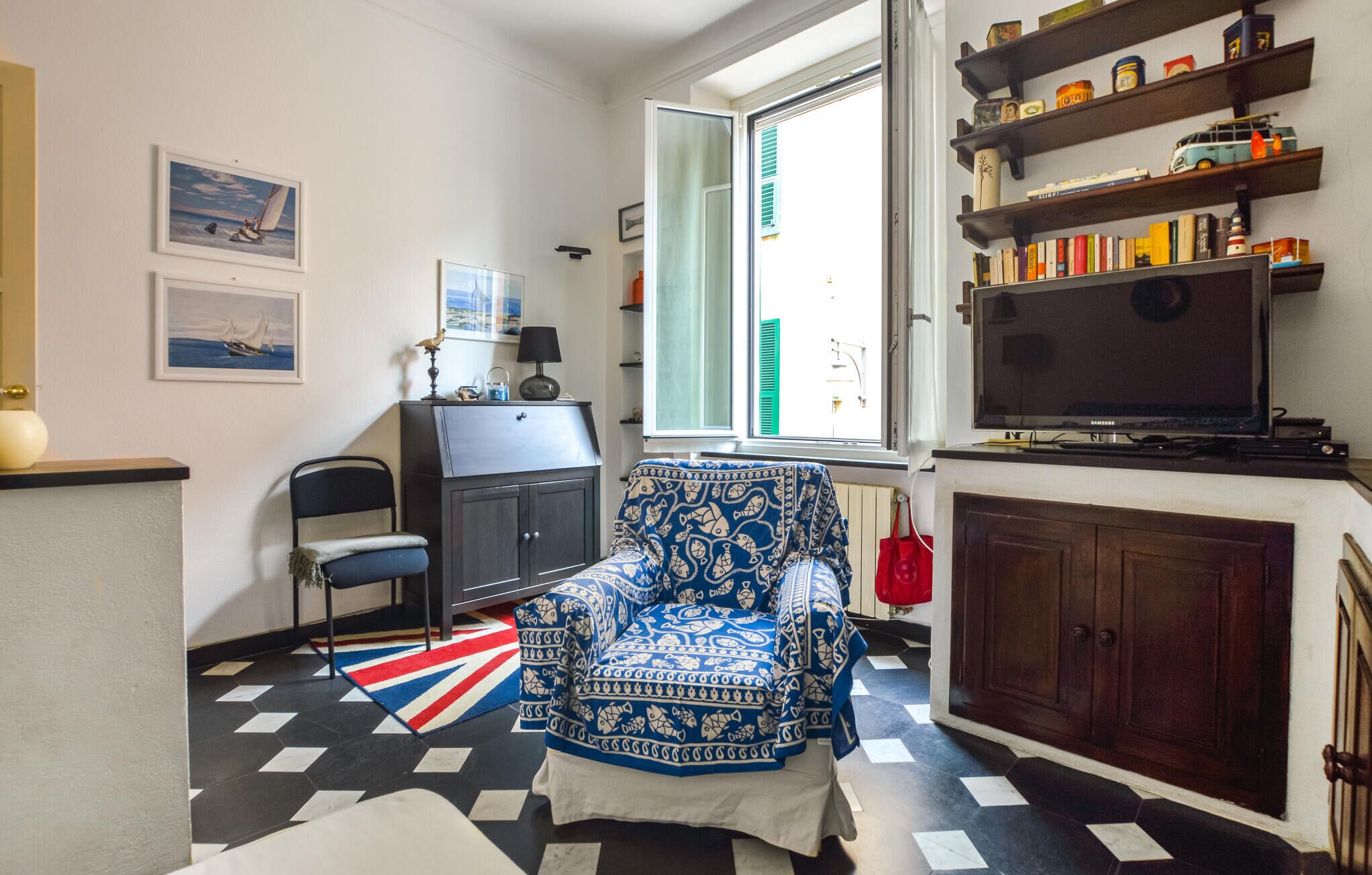Una sala de estar con un sillón estampado, un televisor y una estantería con diversos objetos.