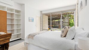 Relax in this serene bedroom with a large bed, shelving unit, and sliding glass door leading to an outdoor area.