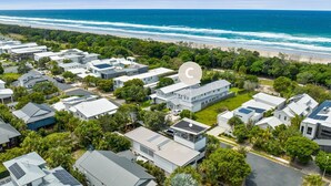 Vista aerea di una zona residenziale con case moderne, pannelli solari e una spiaggia sullo sfondo.