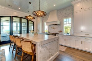 A spacious kitchen with a large island, white cabinetry, and a modern stove.