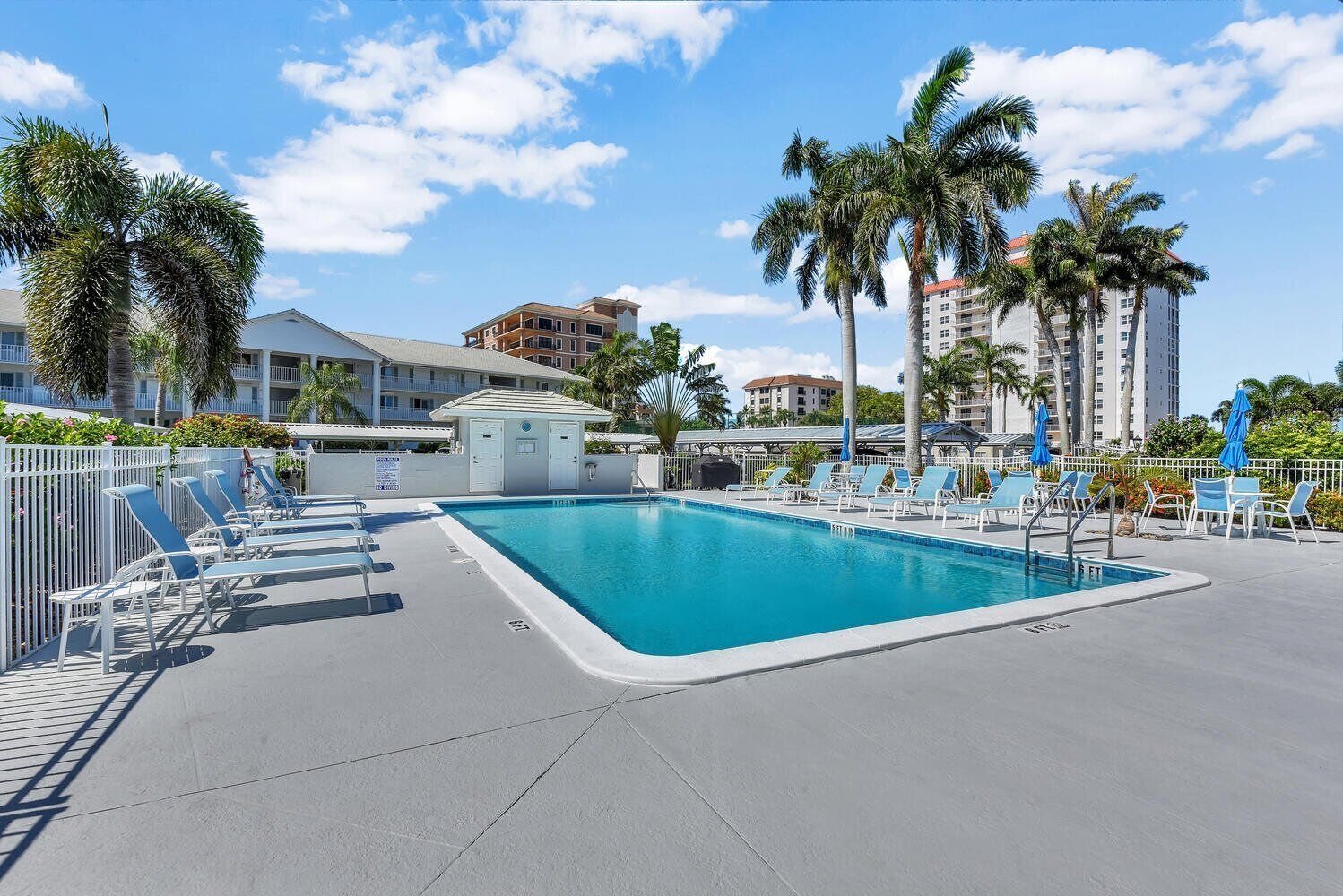 Une piscine entourée de bâtiments d’hôtel, avec des chaises longues et des palmiers.