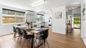A modern kitchen with white cabinets, a dining area with a wooden table and black chairs, and a view of greenery outside. - Trail Side Cottage (Clare)