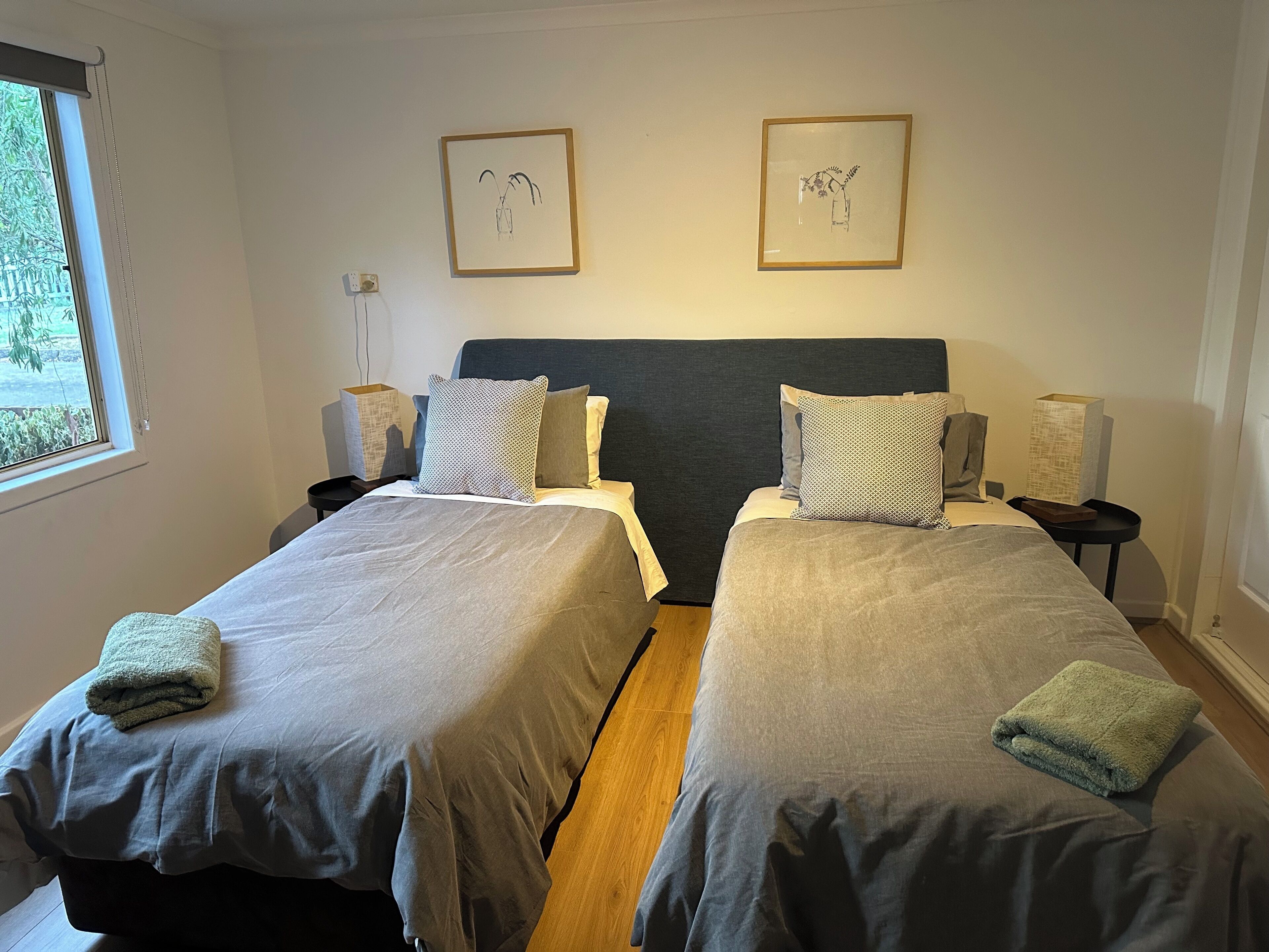 Une chambre avec un lit double, deux lits simples, une table de chevet avec une lampe et deux tableaux encadrés au mur.