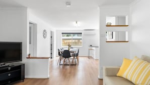 A modern living room with a flat-screen TV, a sofa with a striped cushion, and a dining area with a table and chairs. - Trail Side Cottage (Clare)