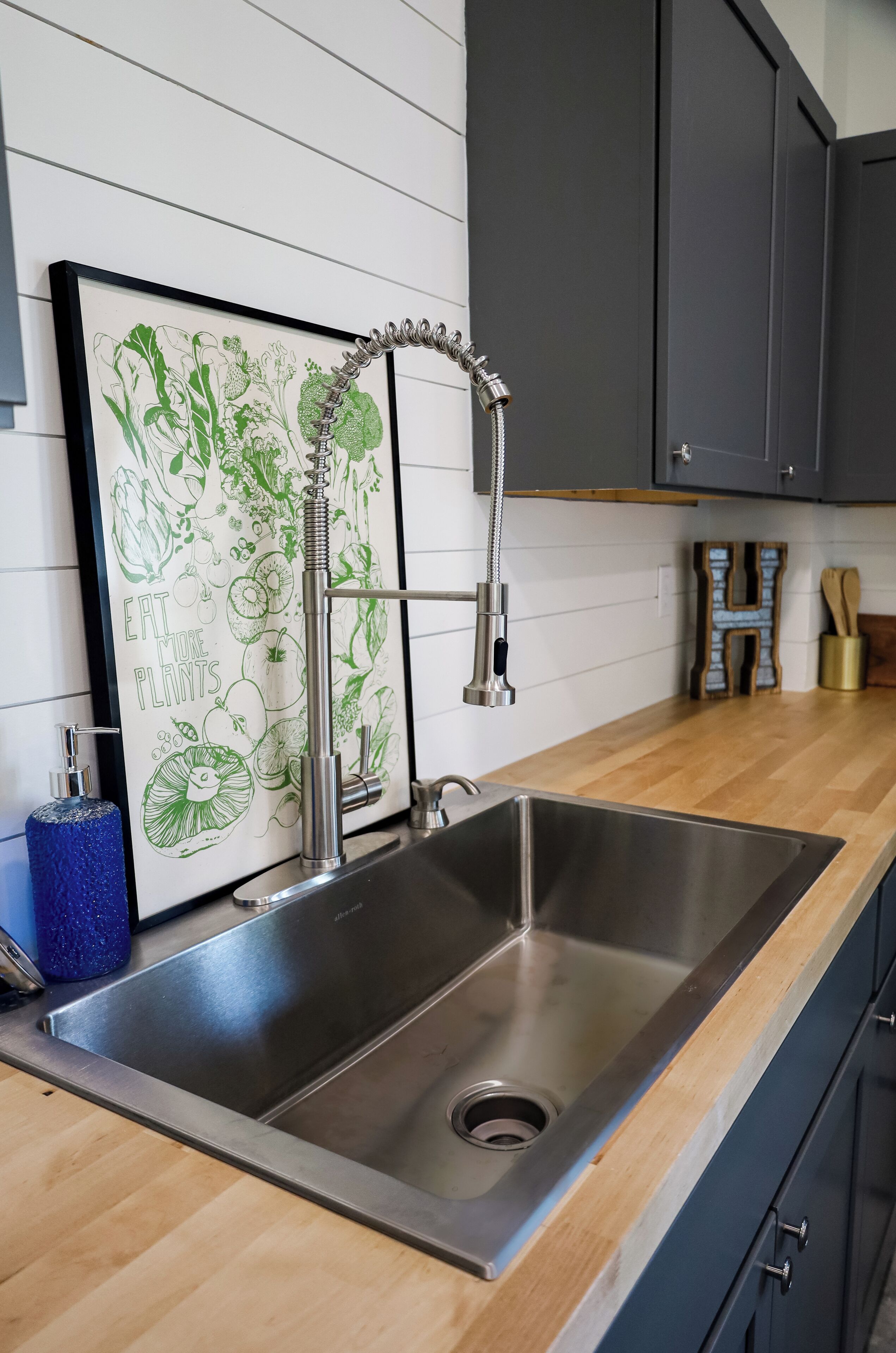 A kitchen with a stainless steel sink, a framed botanical illustration, and wooden cabinets.