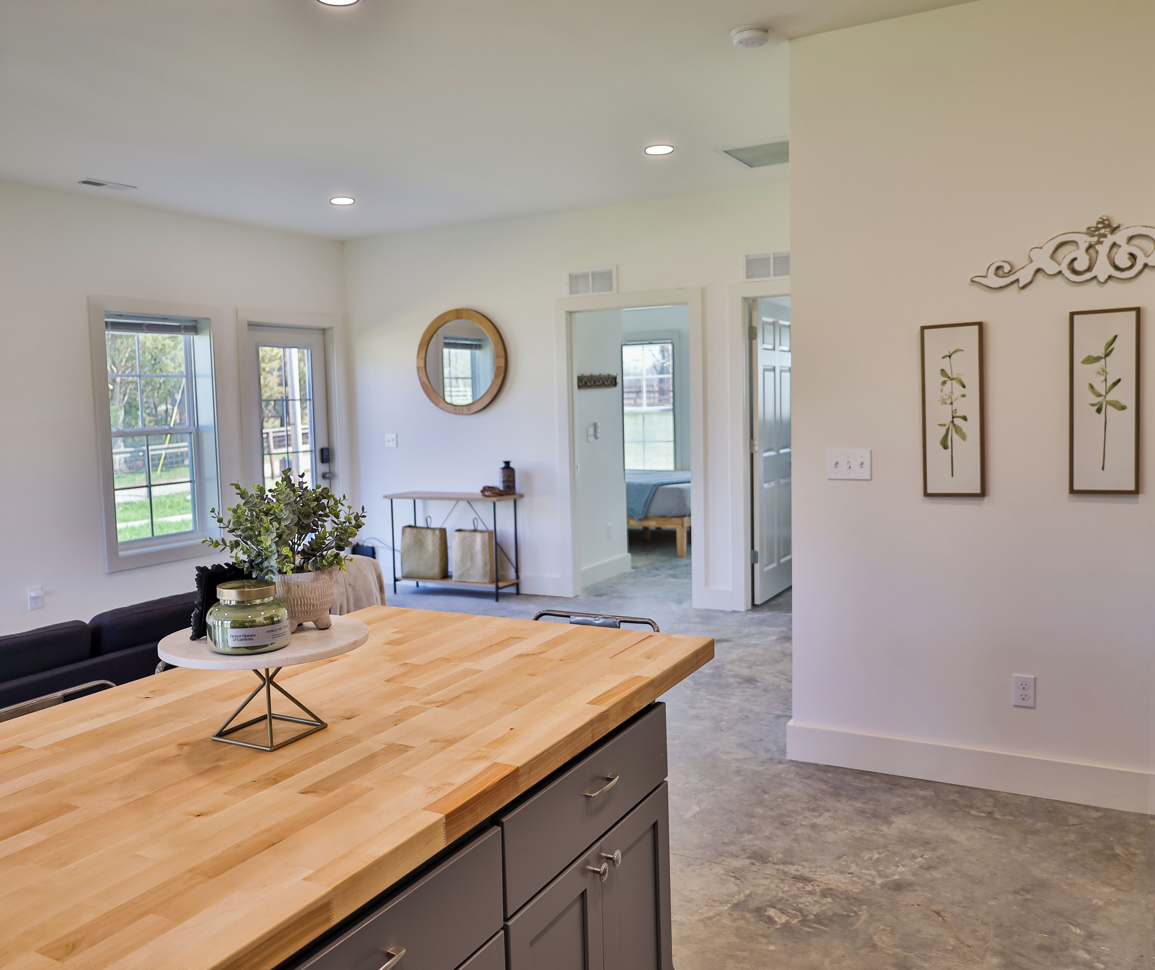 A modern kitchen with a wooden countertop, a round mirror, and a view to the dining area.