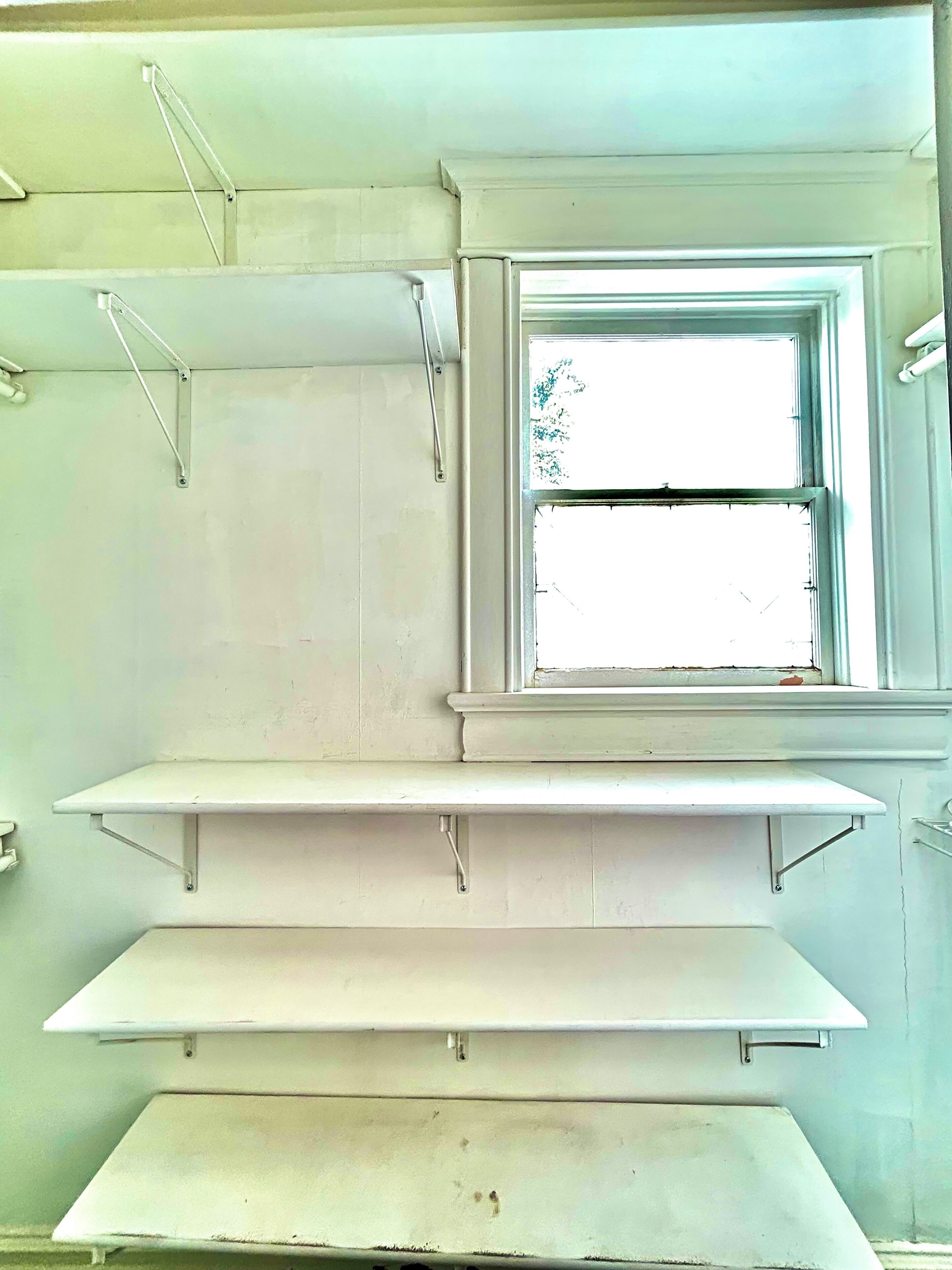 Ein Zimmer mit Fenster, weißen Wänden und drei an der Wand befestigten Regalen.