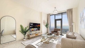 Ein modernes Wohnzimmer mit großem Flachbildfernseher, bequemen Sitzmöglichkeiten, einem Couchtisch und einem großen Fenster mit Blick auf die Stadt.