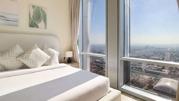 Ein Schlafzimmer mit großem Fenster, einem Bett mit gemusterten Kissen, einem Nachttisch und Blick auf die Stadt.