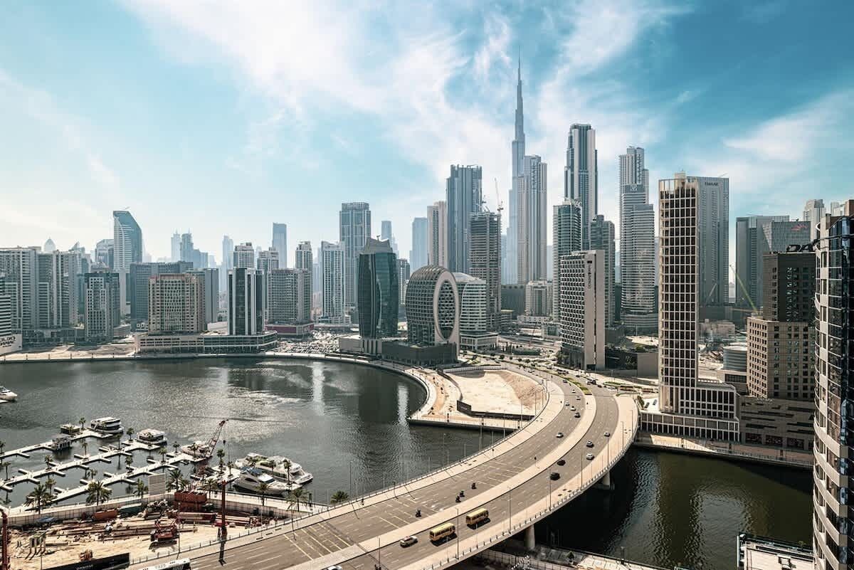A cityscape with high-rise buildings, a marina, and a curved road.