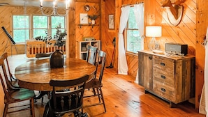 L’intérieur d’un chalet en bois, avec une table à manger, des chaises, un lustre, une radio et une tête de cerf accrochée au mur.