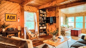 L’intérieur d’un chalet confortable, avec un canapé en cuir, un fauteuil à bascule, une table basse en bois et une bibliothèque.