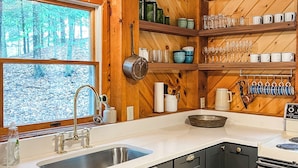 Une cuisine avec des meubles de rangement en bois, un évier et une cuisinière. On y trouve des étagères remplies d’assiettes et de verres.