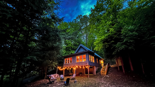 Une maison en bois à deux étages, dotée d’un porche et entourée d’arbres.