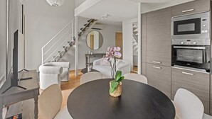 A modern kitchen with a built-in microwave and oven, a round dining table with chairs, and a staircase leading to another level. - Charming Family Duplex in a Peaceful Residence (Cannes)