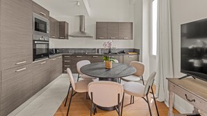 A modern kitchen with a dining area, featuring a round table, chairs, and a TV. - Charming Family Duplex in a Peaceful Residence (Cannes)