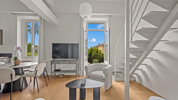 A modern living room with a TV, dining area, and a staircase. - Charming Family Duplex in a Peaceful Residence (Cannes)