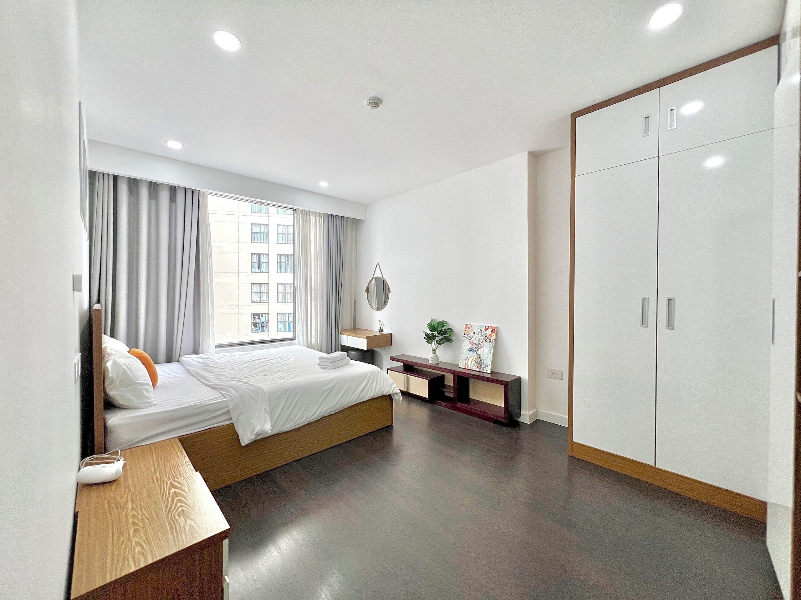 Una habitación de hotel moderna con una cama grande, una mesita de noche, un espejo, un escritorio pequeño y un armario.