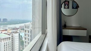A hotel room with a large window, a bed, a bedside table with a vase, and a wall-mounted mirror. - Golden Apartment (Ho Chi Minh City)