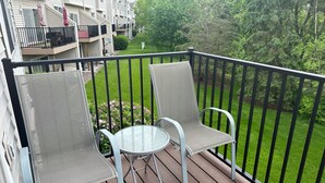Ein Balkon mit zwei Stühlen und einem kleinen Tisch mit Blick auf einen gepflegten Rasen und angrenzende Gebäude.
