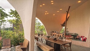 Uma sala de jantar integrada com uma mesa de madeira comprida, bancos e um espaço de bar com banquetas.