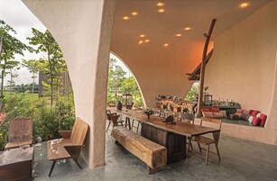 Un comedor de concepto abierto con una larga mesa de madera, bancos y una zona de bar con taburetes.
