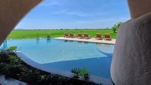 Piscina com espreguiçadeiras e vista para um campo verde.