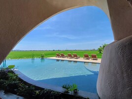 Una piscina con sillones de descanso y vistas a un campo verde.