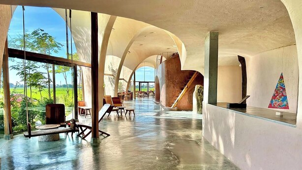 Interior espaçoso e moderno, com teto curvo e grandes janelas que dão vista para uma paisagem verde.