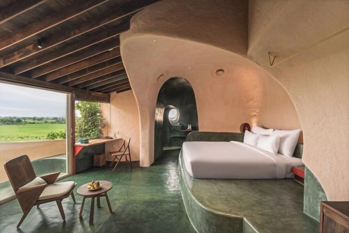 Un dormitorio con techo curvo, una cama, una silla, una mesita y vistas al exterior.