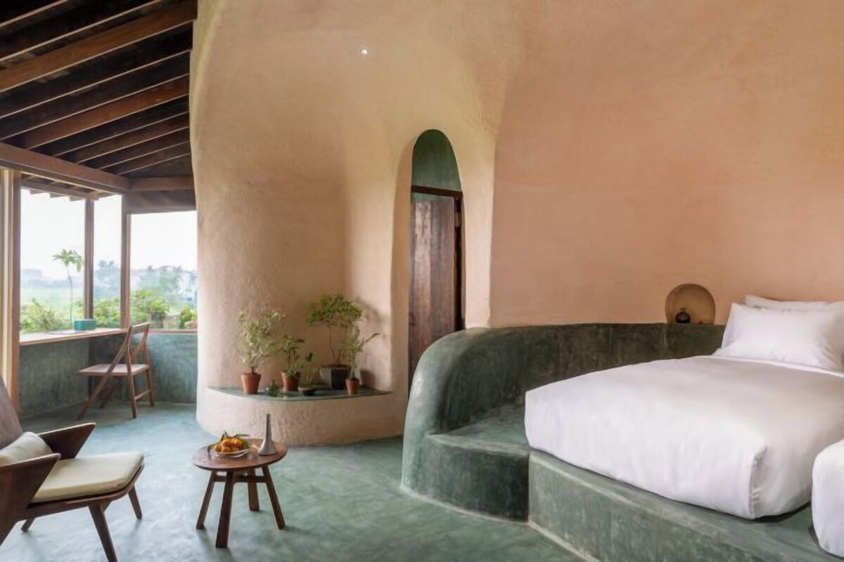 Un dormitorio con cama, una silla, una mesita y una planta en maceta.