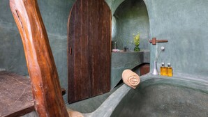 Um banheiro com porta de madeira, pia, toalha e duas garrafas de líquido.