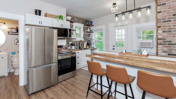 Een moderne keuken met roestvrijstalen apparatuur, een houten kookeiland met barkrukken, en een wand van baksteen.