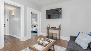 Een woonkamer met een houten salontafel, een grijze bank en een flatscreen televisie die aan de muur is bevestigd.