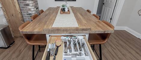 A wooden dining table with a tray of cutlery and a placemat in the center.