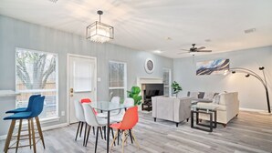A modern living room with a fireplace, a dining area with a glass table, and a sofa. - Stylish Modern House  4BR/3BA  Home in McKinney (McKinney)