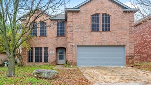 A two-story brick house with a garage, a large tree in the front yard, and a stone pathway leading to the entrance. - Stylish Modern House  4BR/3BA  Home in McKinney (McKinney)