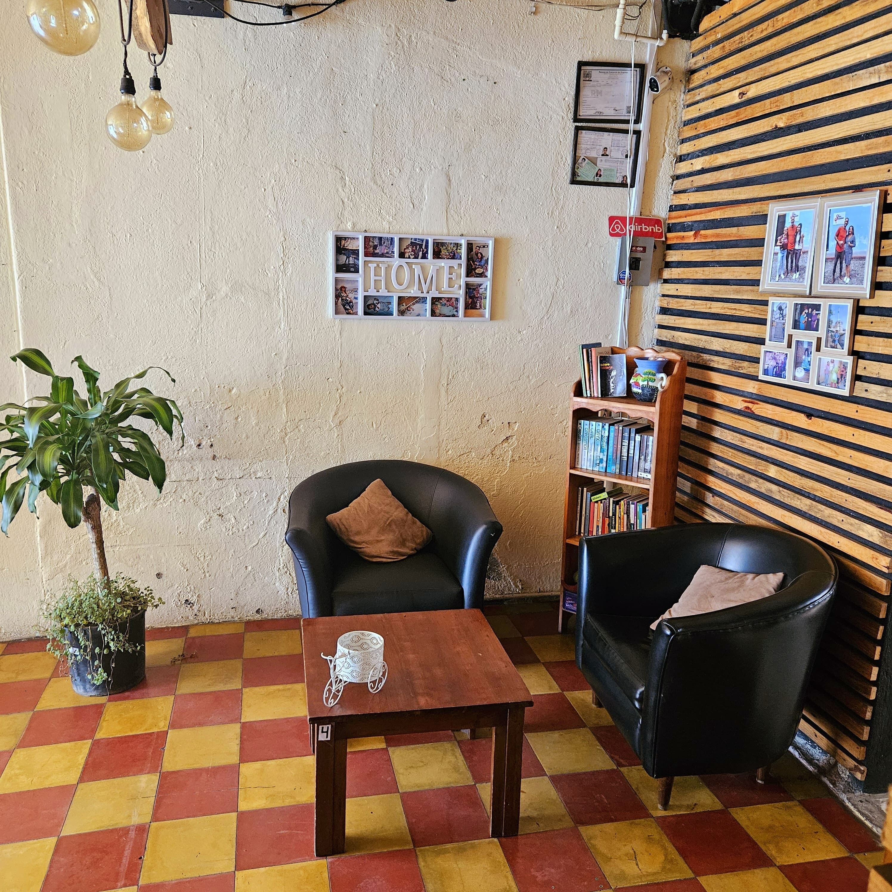 Ein gemütliches Zimmer mit kariertem Boden, einem Bücherregal, einem Ledersessel und einem kleinen Tisch mit einer Dekoration.