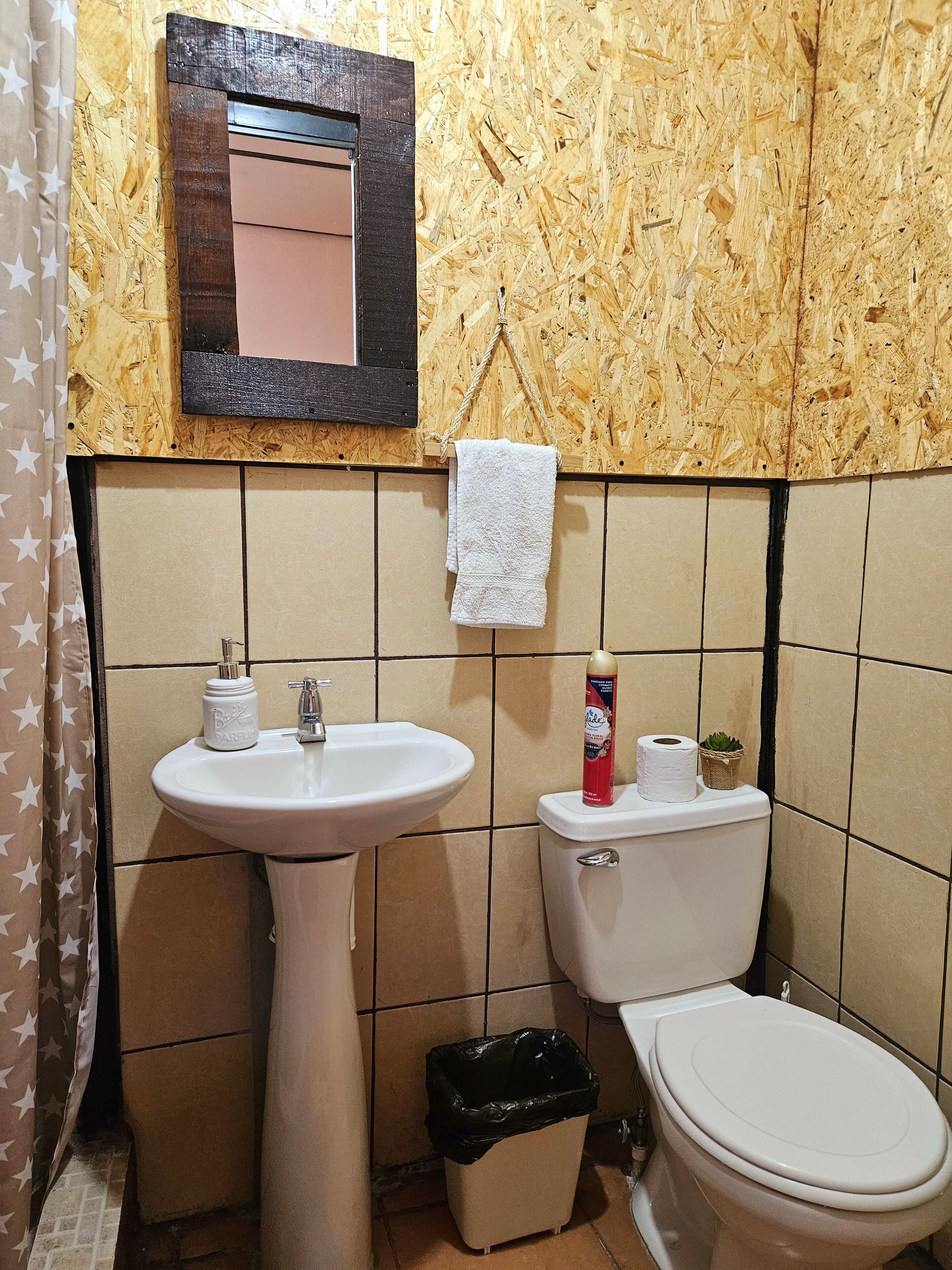 Baño con pared de madera, lavamanos, inodoro y cubo de basura.