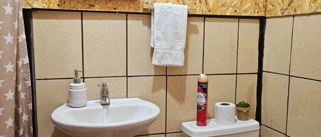 Baño con pared de madera, lavamanos, inodoro y cubo de basura.