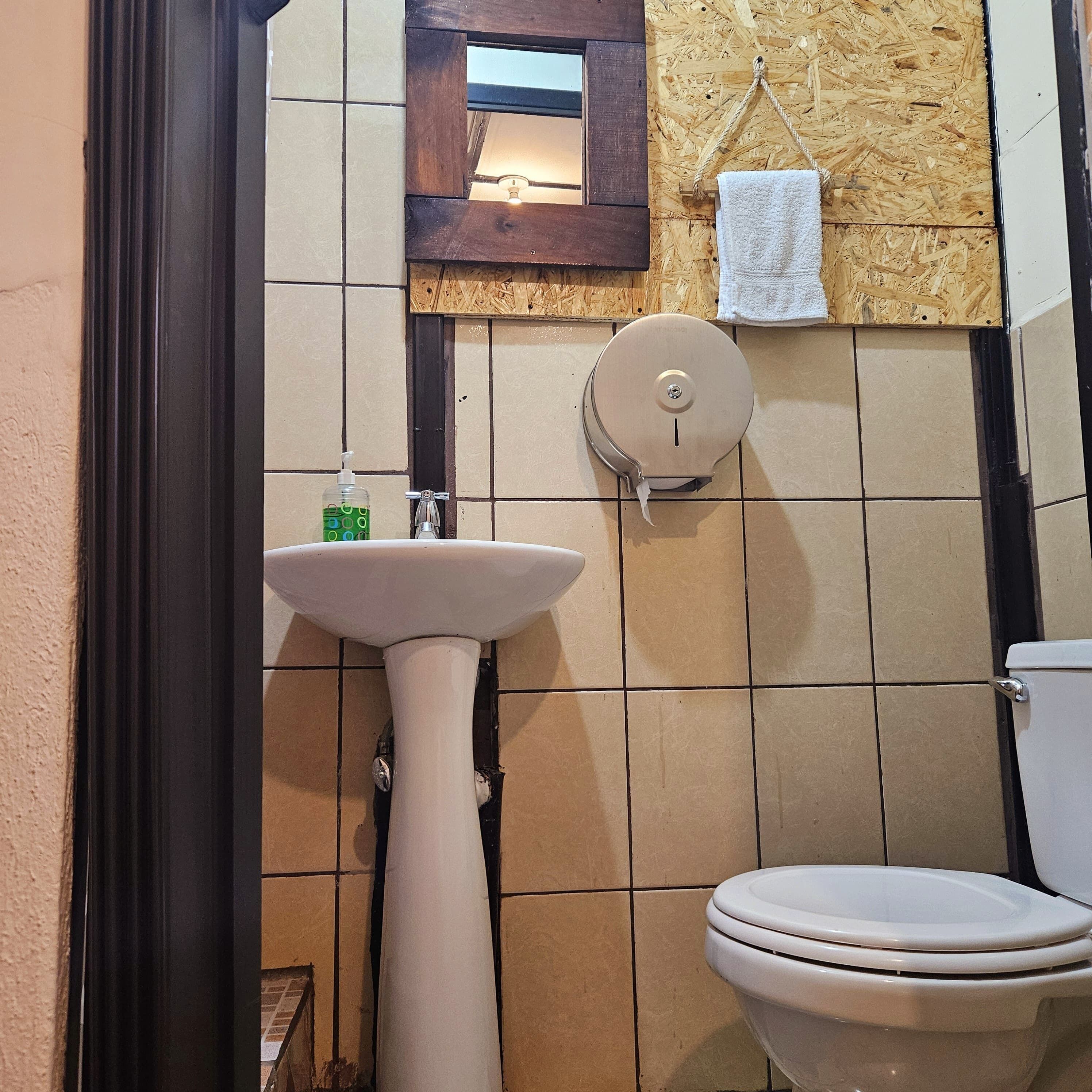 Een badkamer met een wastafel op een zuil, een toilet en een spiegel boven de wastafel.