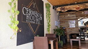 Un restaurant avec une enseigne indiquant « Cermeno’s House Restaurant & Hotel ». On y trouve des chaises et des tables, ainsi qu’un sol à carreaux.
