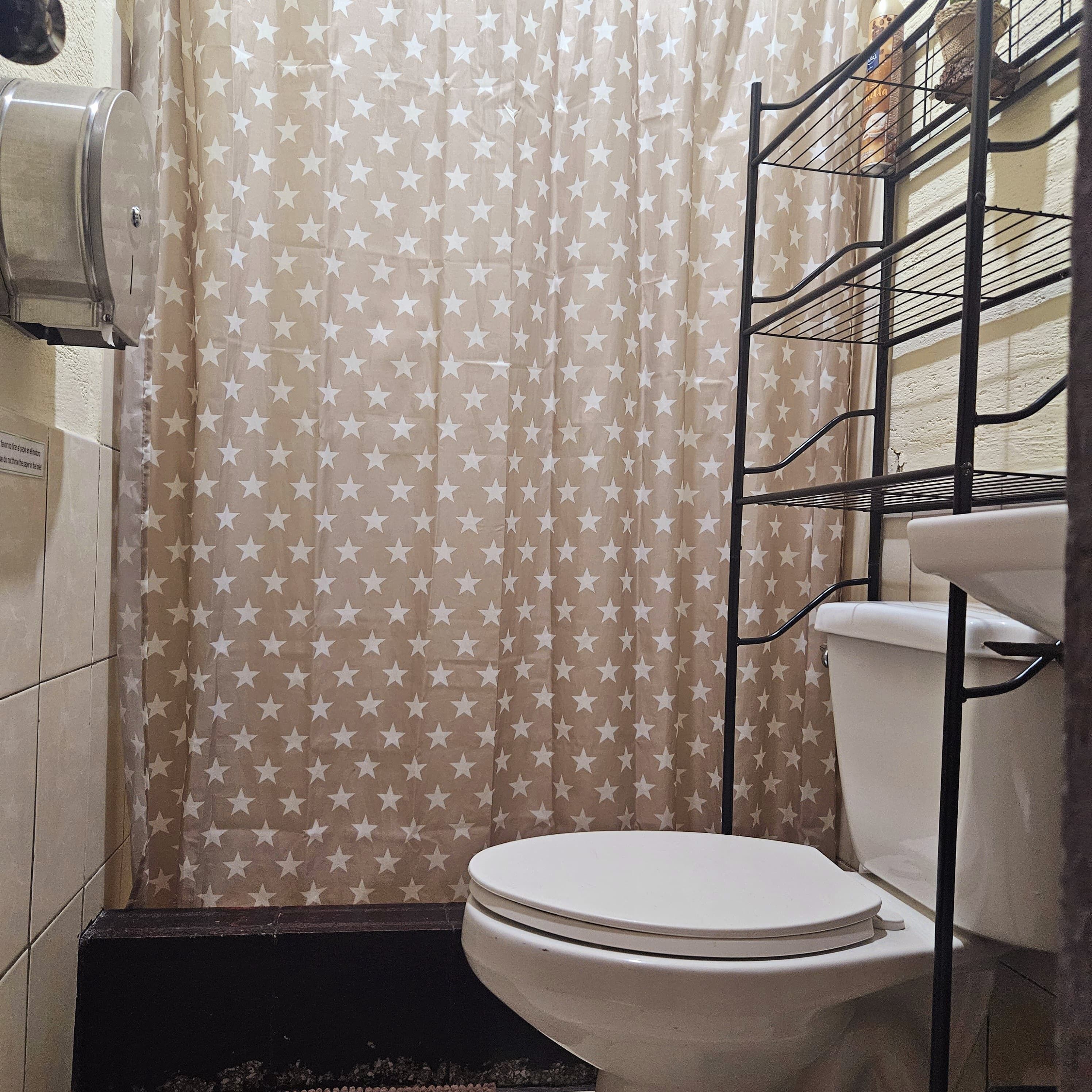 A bathroom with a toilet, a shower curtain with a star pattern, and a metal shelf unit.