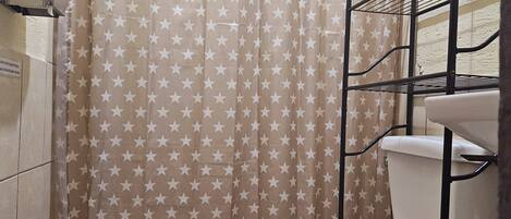 A bathroom with a toilet, a shower curtain with a star pattern, and a metal shelf unit.