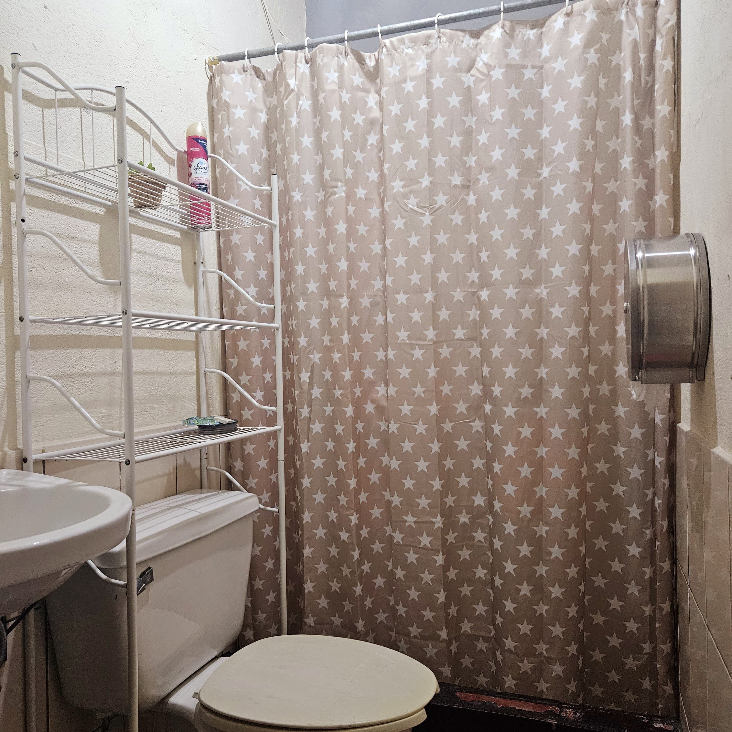 Un baño pequeño con inodoro, un estante con artículos de aseo y cortina de ducha con estampado de estrellas.