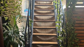 Un escalier en bois avec des rampes en métal, entouré de plantes en pot et d’un mur en bois.