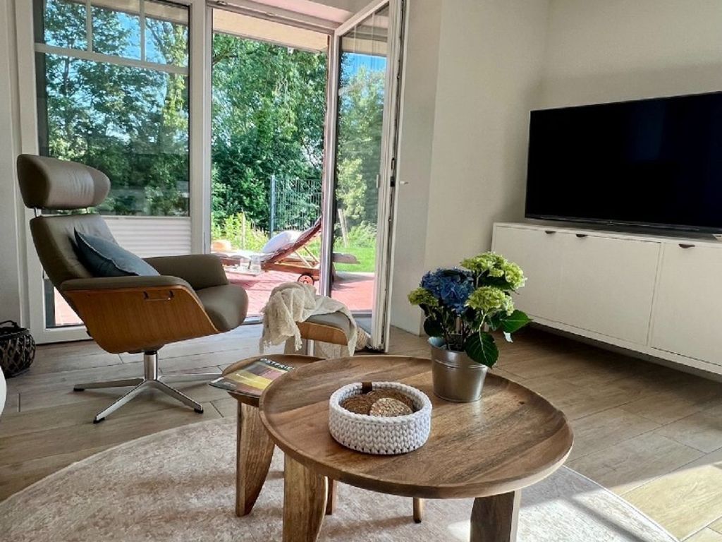 Uma sala de estar moderna com uma televisão grande, uma poltrona confortável, uma mesinha com uma cama para animais de estimação e um vaso de planta.