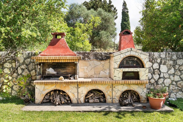 A stone-built outdoor kitchen with a chimney, a fire pit, and a potted plant.