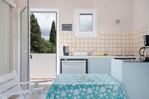 A compact kitchen with a window, a refrigerator, a sink, and a table with a floral tablecloth. - Apartment 'Sea View 1' with Shared Pool, Wi-Fi and Air Conditioning (Kefalonia)