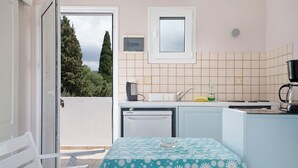 Une cuisine de taille réduite, dotée d’une fenêtre, d’un réfrigérateur, d’un évier et d’une table recouverte d’une nappe à motifs floraux.
